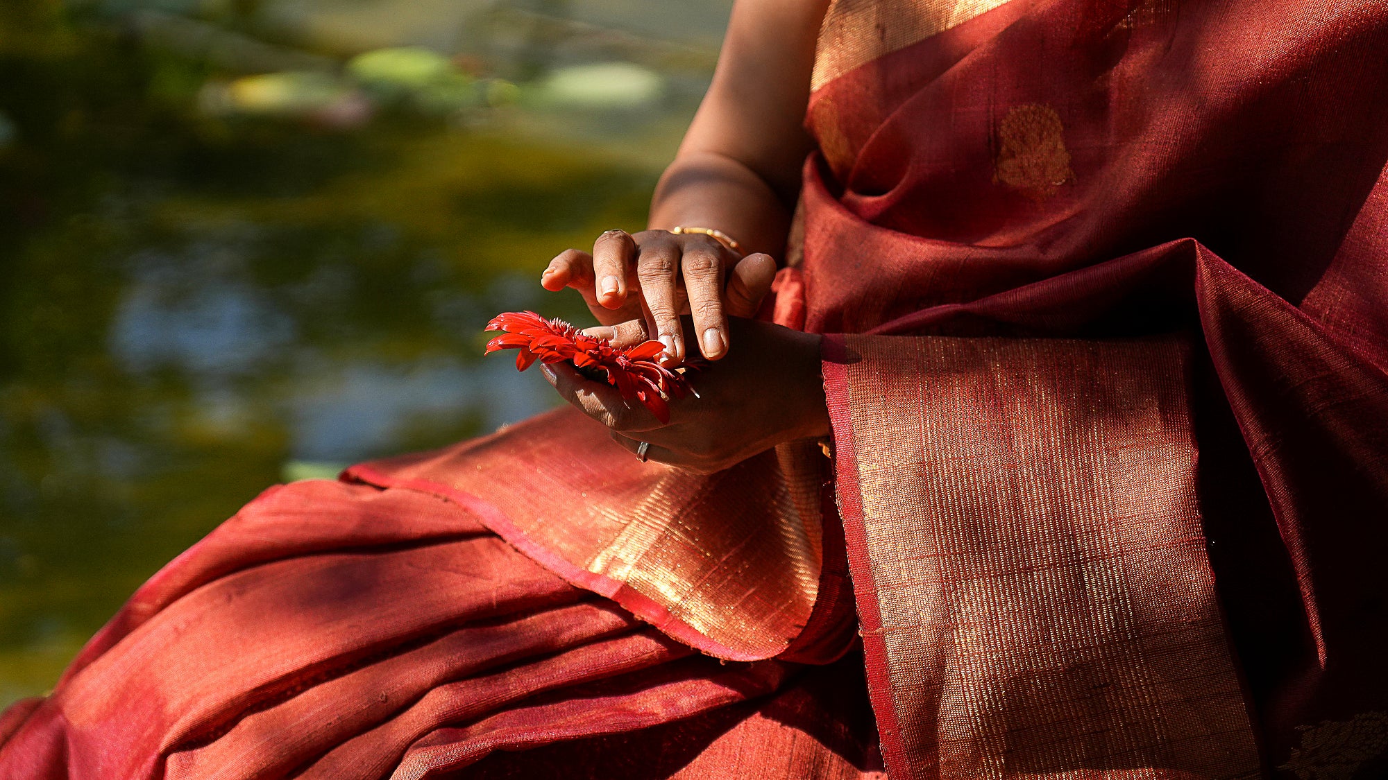 Woman wearing a red Raw Silk handloom saree holding a flower