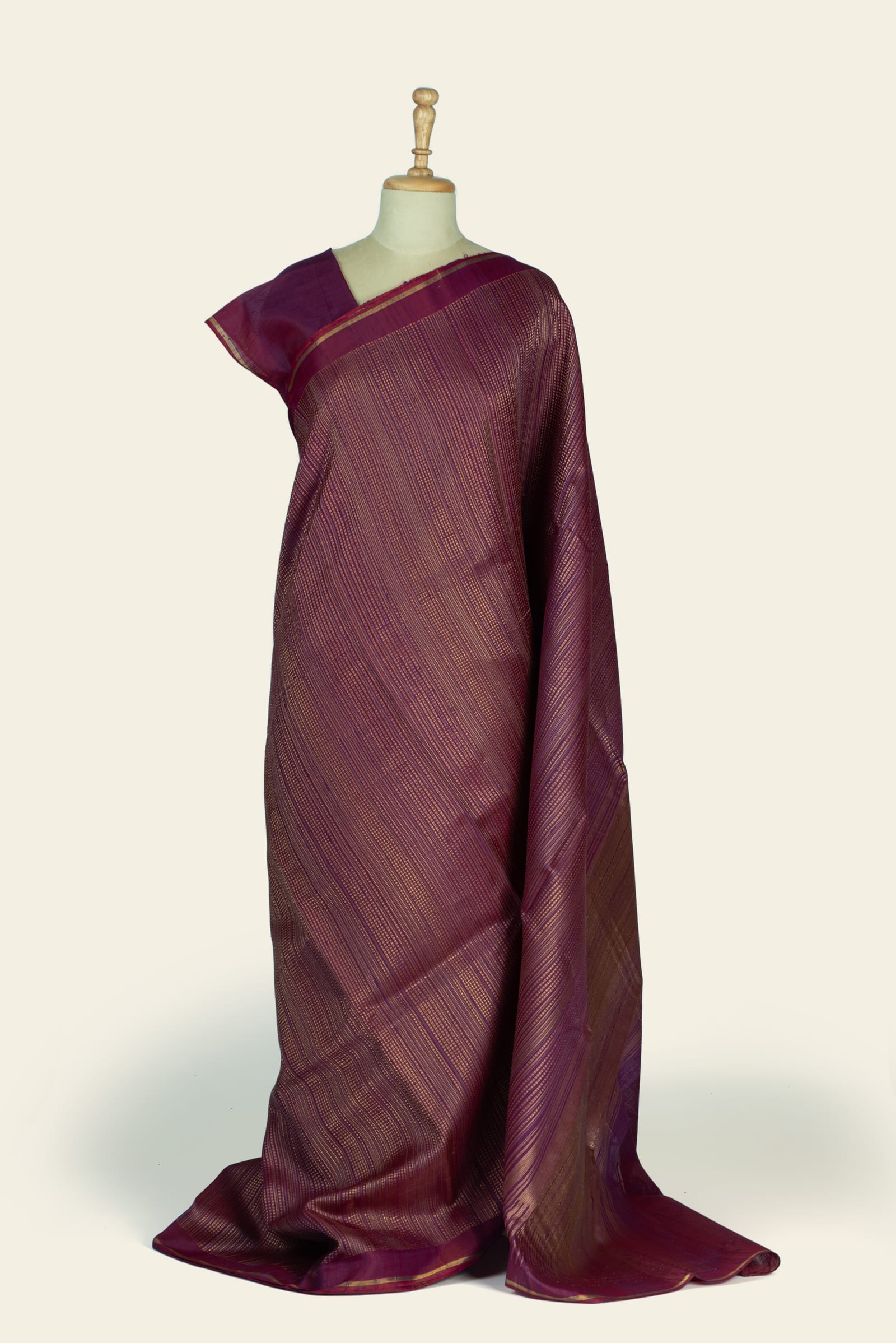 Full-length drape of a plum purple saree shown on a mannequin with subtle stripe pattern and a narrow gold-bordered edge.