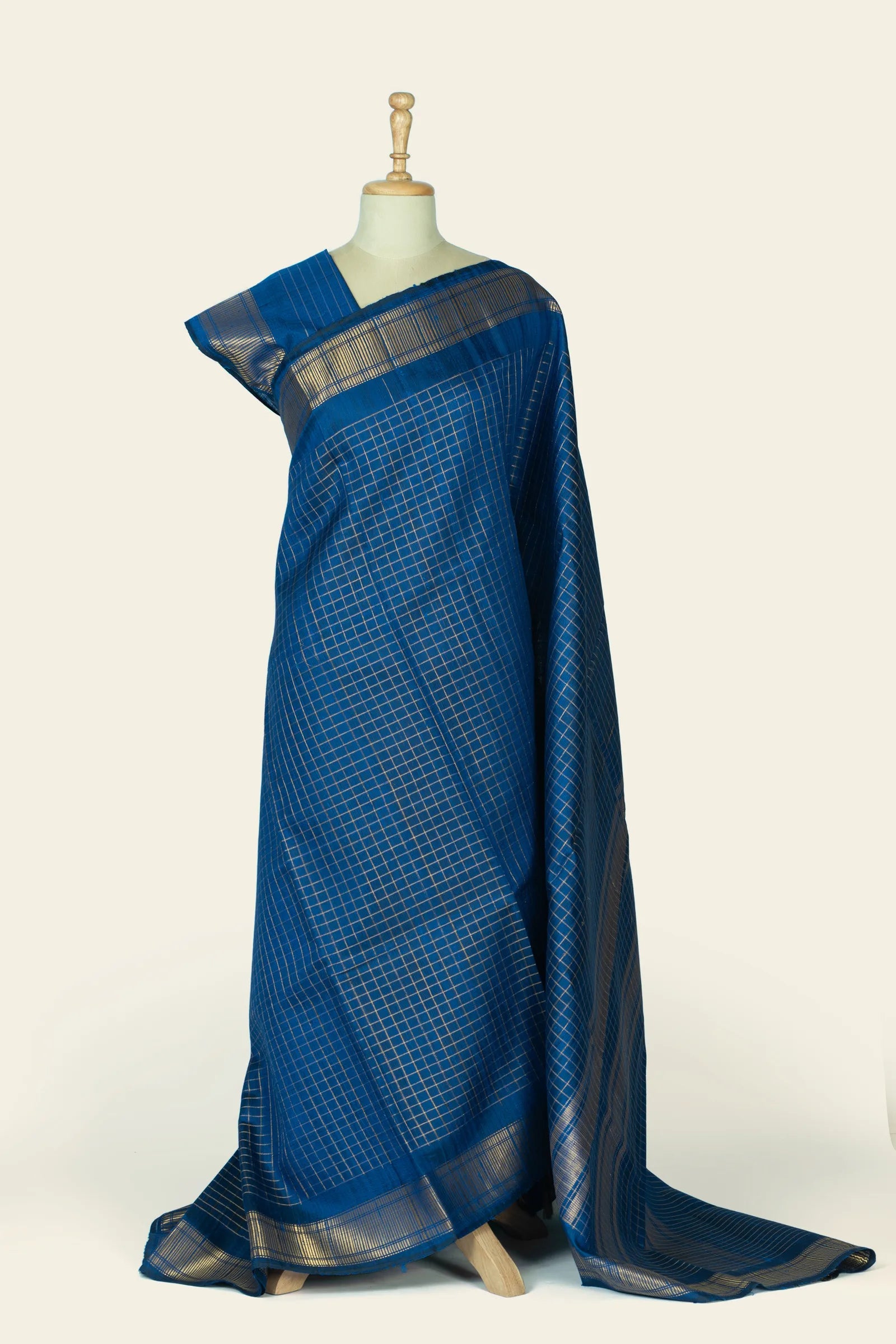 Full-length drape on a mannequin showing an indigo blue saree with a fine checked grid over the body and a broad metallic striped border at the hem.