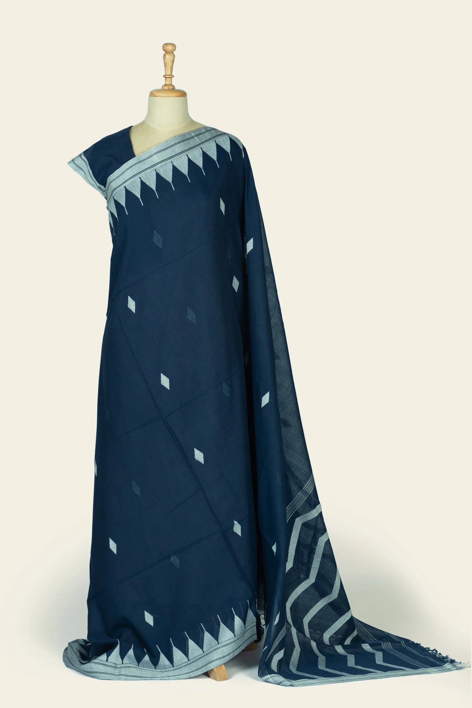 Full-length drape of an indigo blue saree on a mannequin showing scattered light-blue diamond buta across the body and a light-blue triangular border at the lower edge.