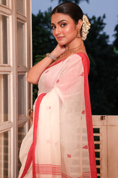 Woman wearing a white saree with red border, standing outdoors.