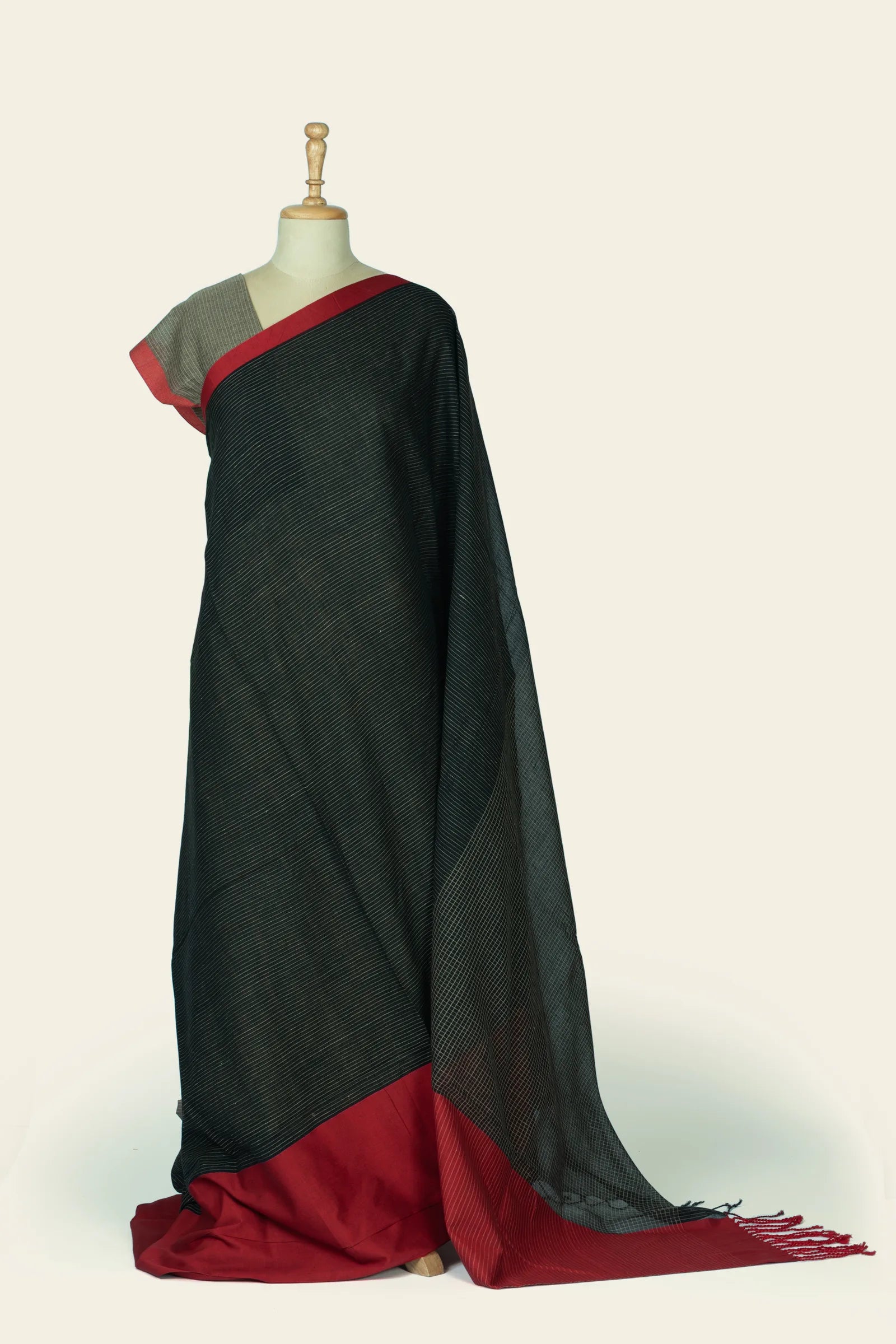 Full-length view of a black saree draped on a mannequin showing fine diagonal pinstripes and a solid red border pooled at the hem.