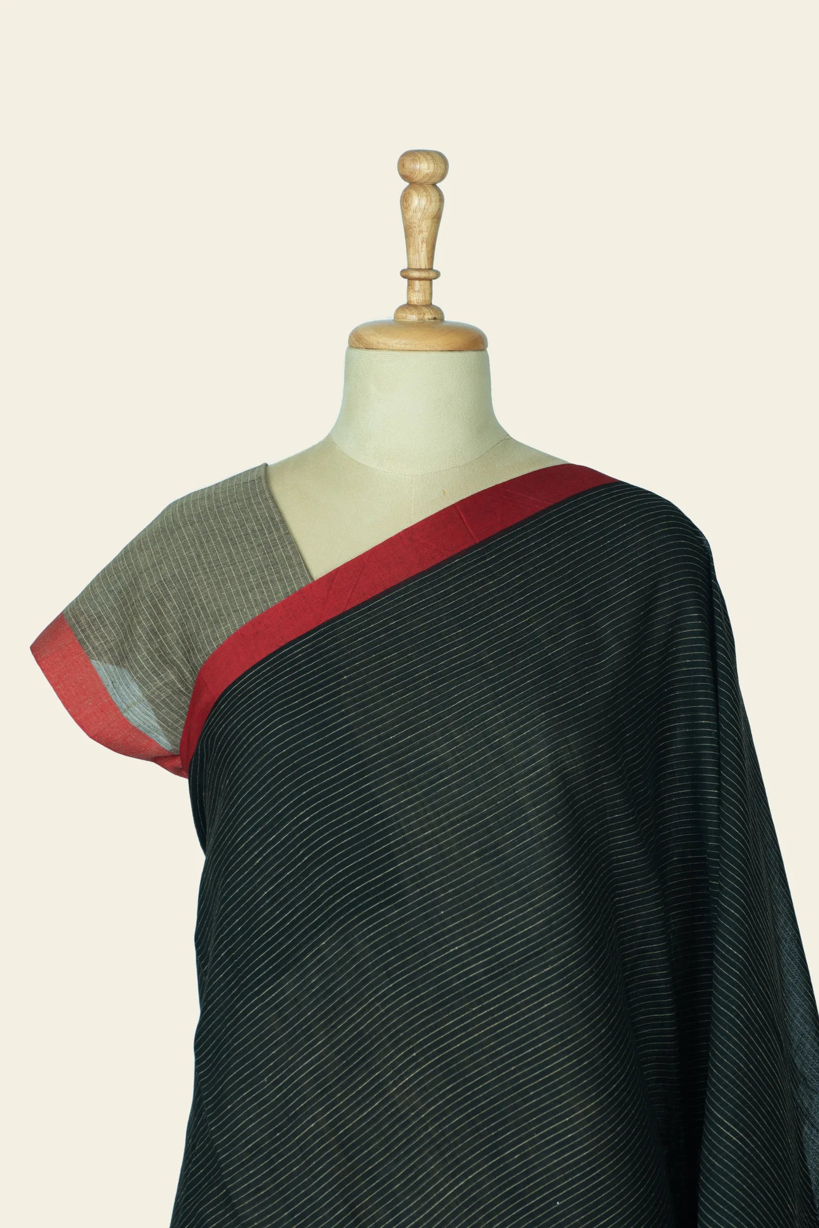 Upper front and shoulder area of the saree on a mannequin showing the red inner border and fine stripes across the body.
