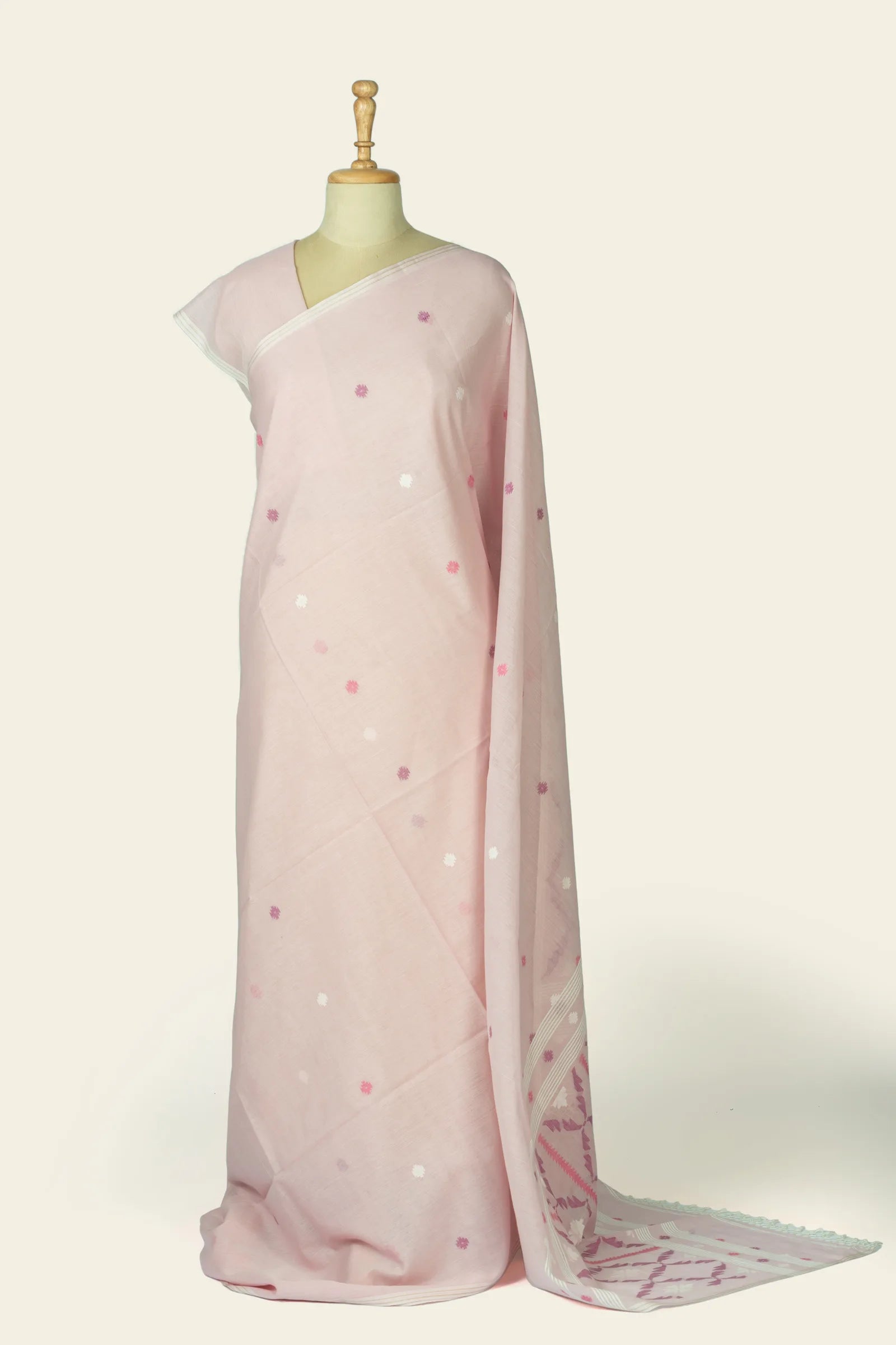 Full-length front drape of a soft pink saree on a mannequin showing scattered small motif dots across the body and the pallu pooling at the floor.