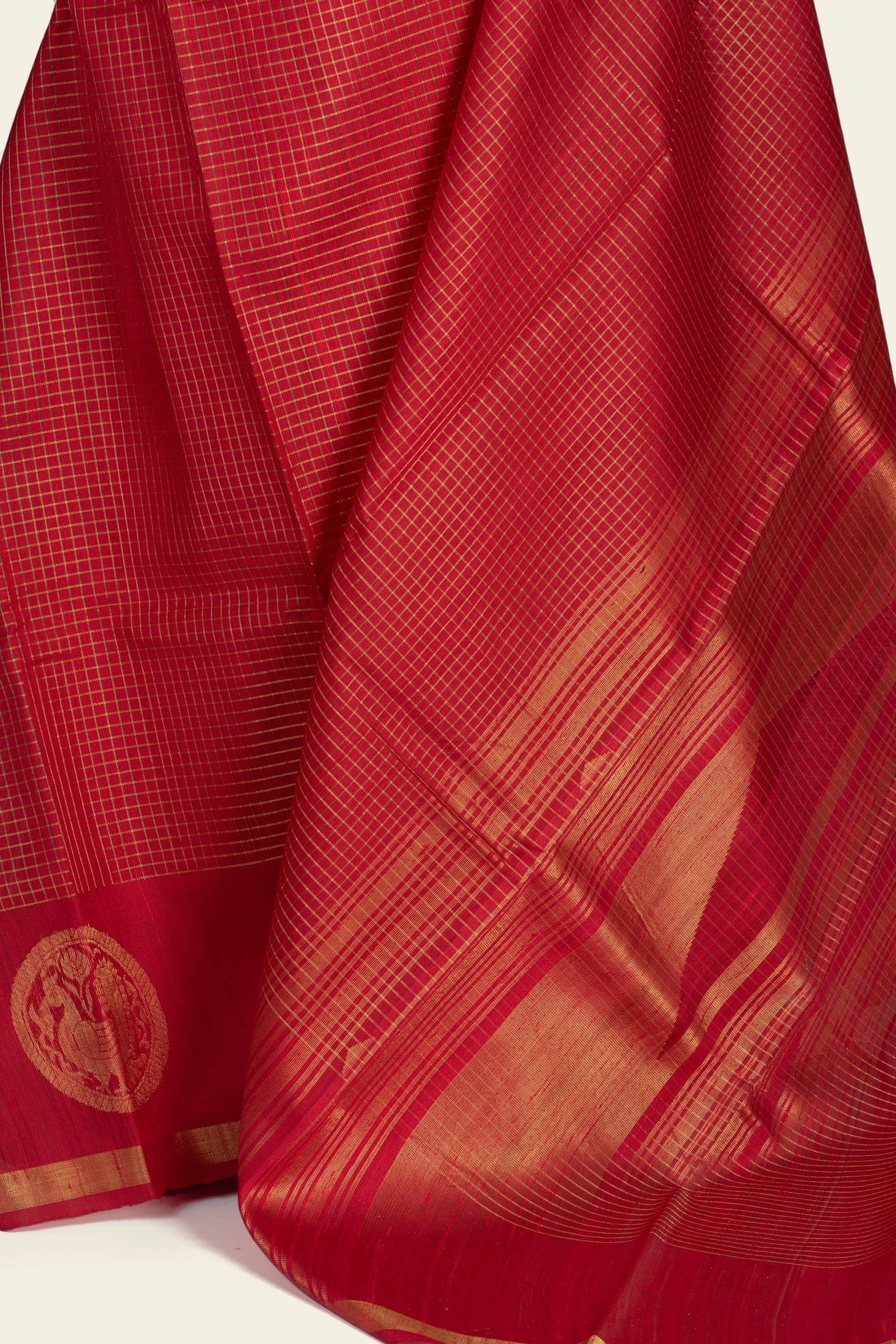Detail of the saree's lower pallu and border showing dense gold stripes and a circular gold medallion motif at the hem.