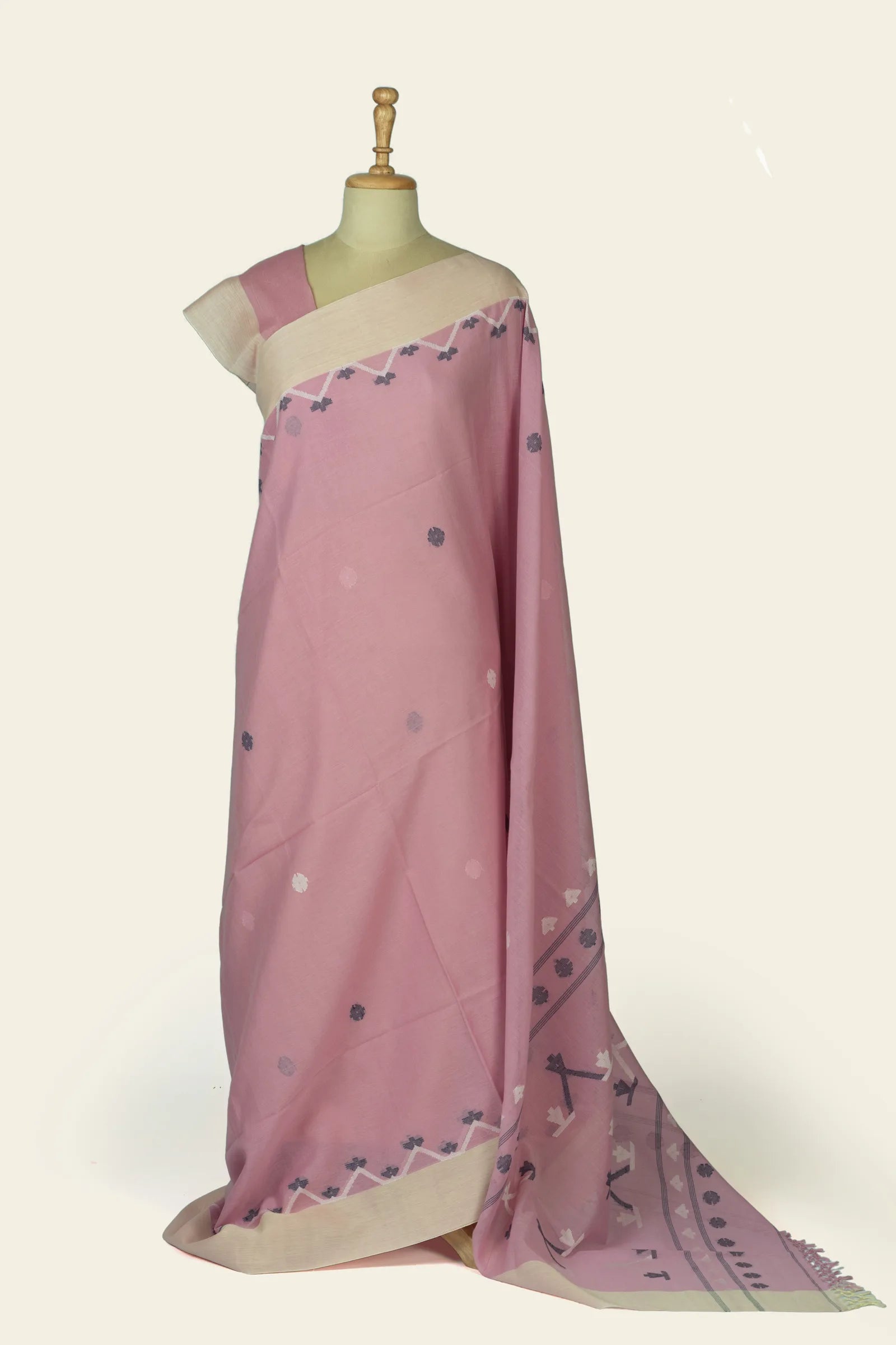 Full drape view of a soft pink saree on a mannequin showing scattered circular buti motifs and a cream contrast border at the hem.