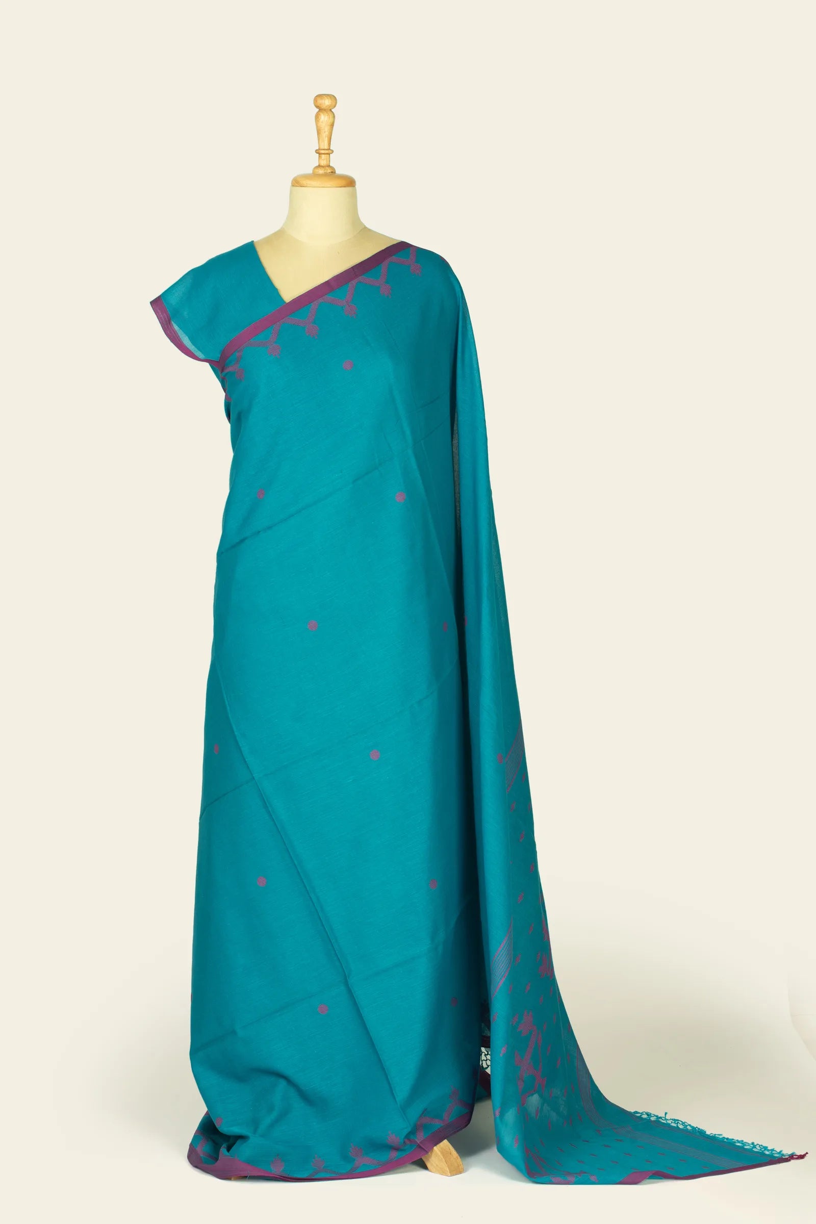 Full-length front view of a teal saree draped on a mannequin showing scattered magenta dots and a narrow magenta border.