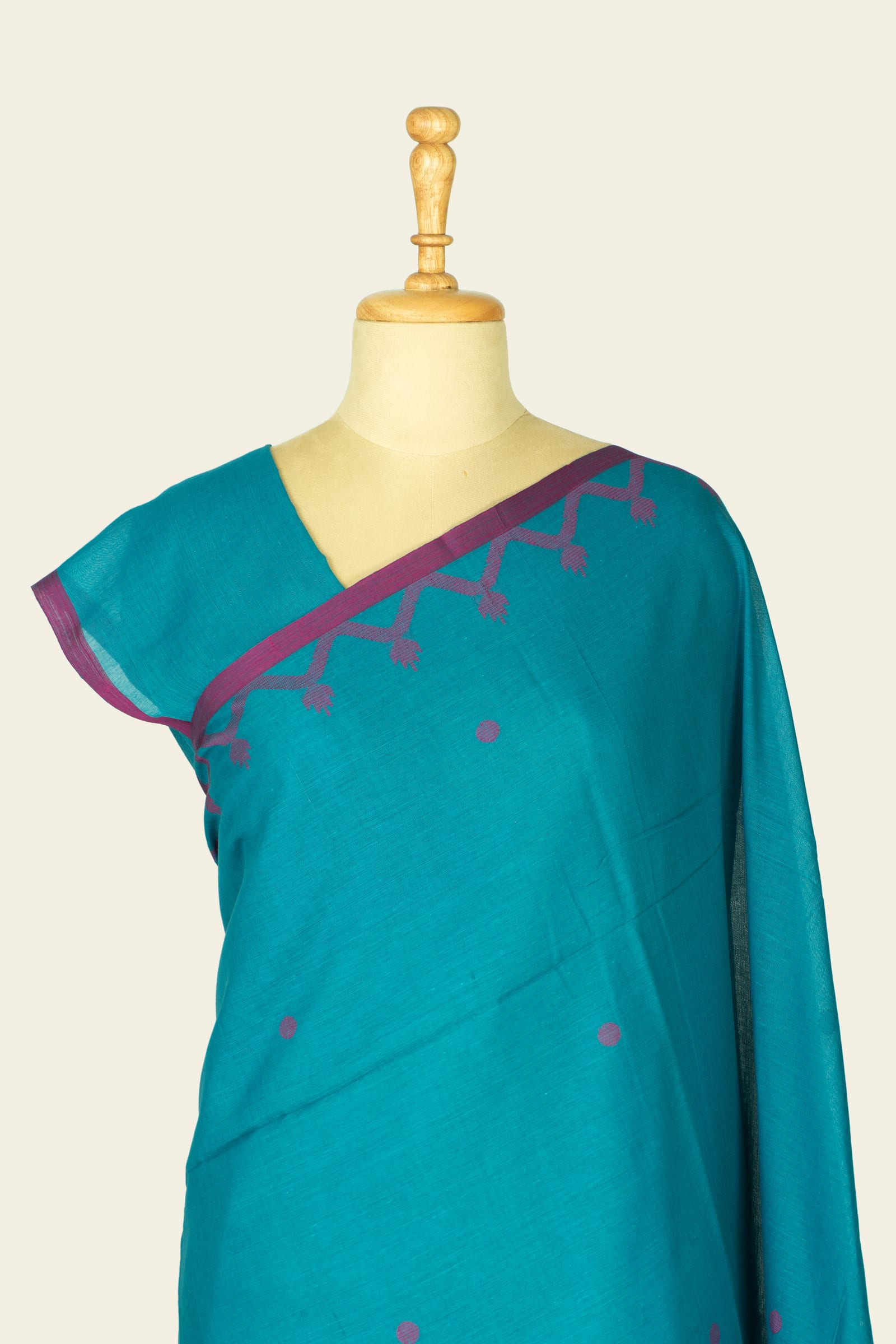 Close front shot of the mannequin showing the saree neckline and small magenta dot motifs on the teal fabric.