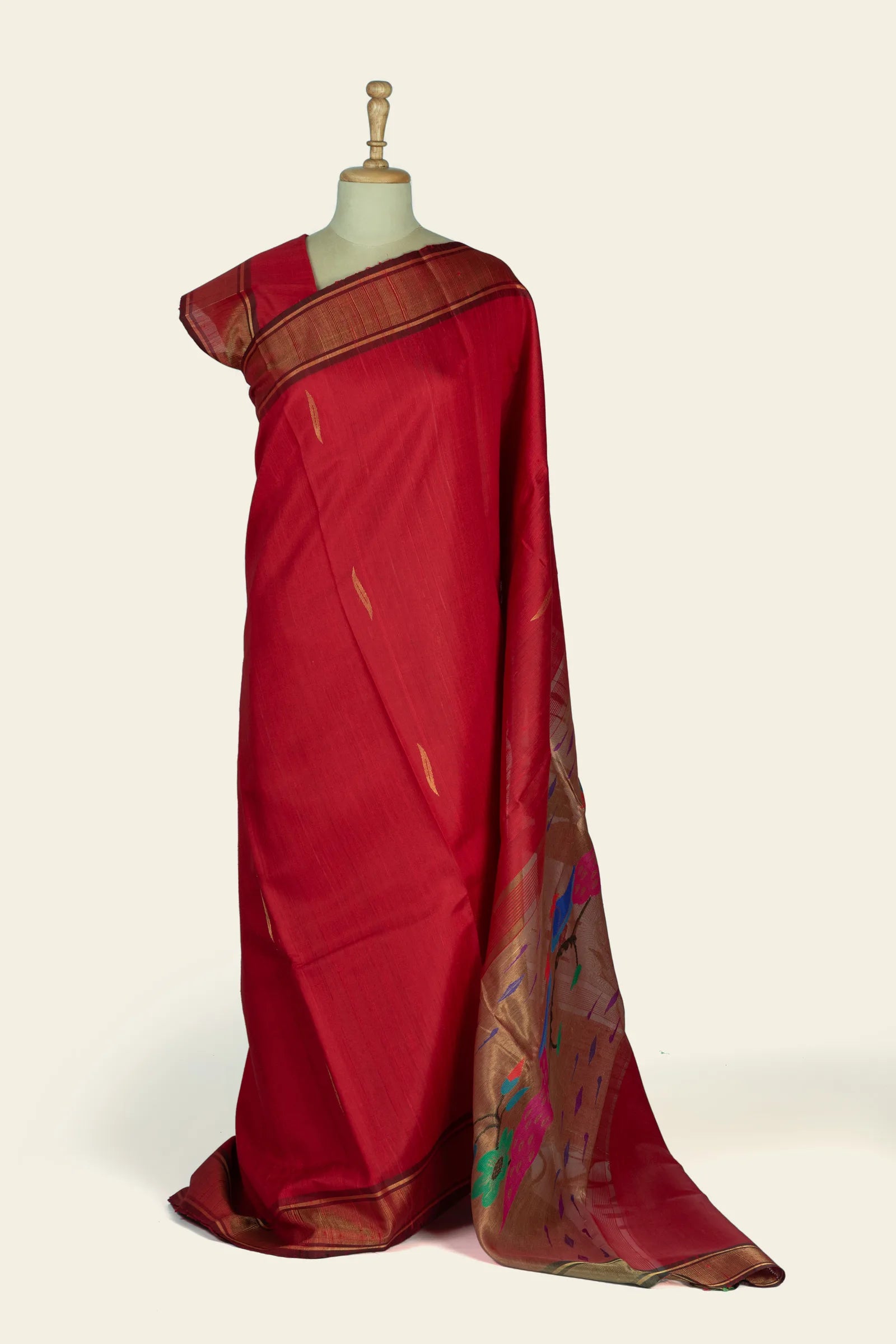 Front drape of a deep red saree showing a narrow gold striped border and small gold buta motifs on the body.