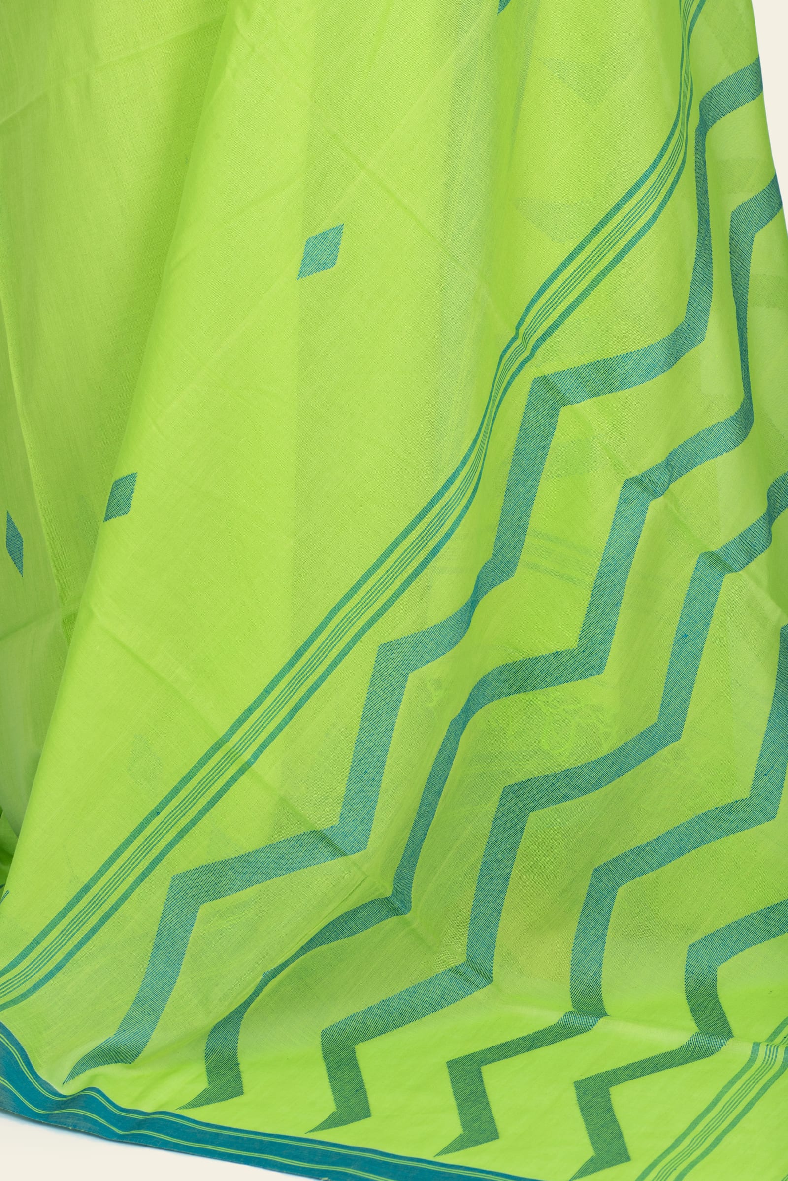Detail of the lower pallu showing a bold teal zig-zag pattern and the saree's striped border with short tassels at the edge.