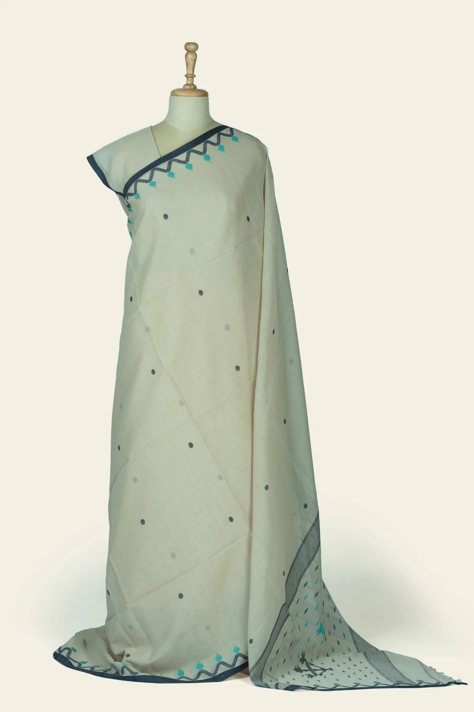 Full-length drape of an ivory saree with small scattered dots and a narrow dark border, pallu pooled at the hem showing patterned edge.