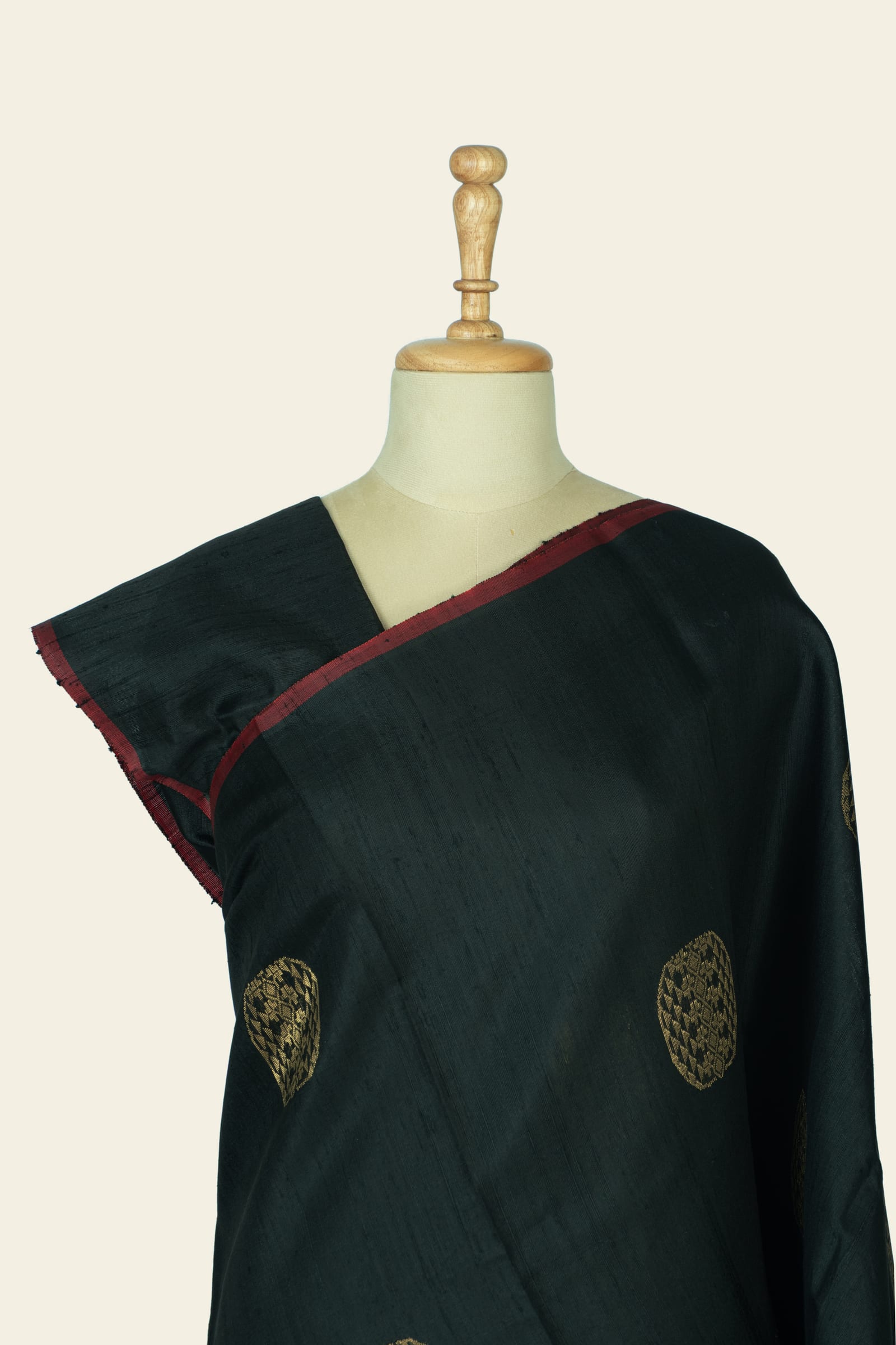 Close-up of the shoulder and upper body showing black fabric, circular gold motifs, and the narrow maroon saree edge.