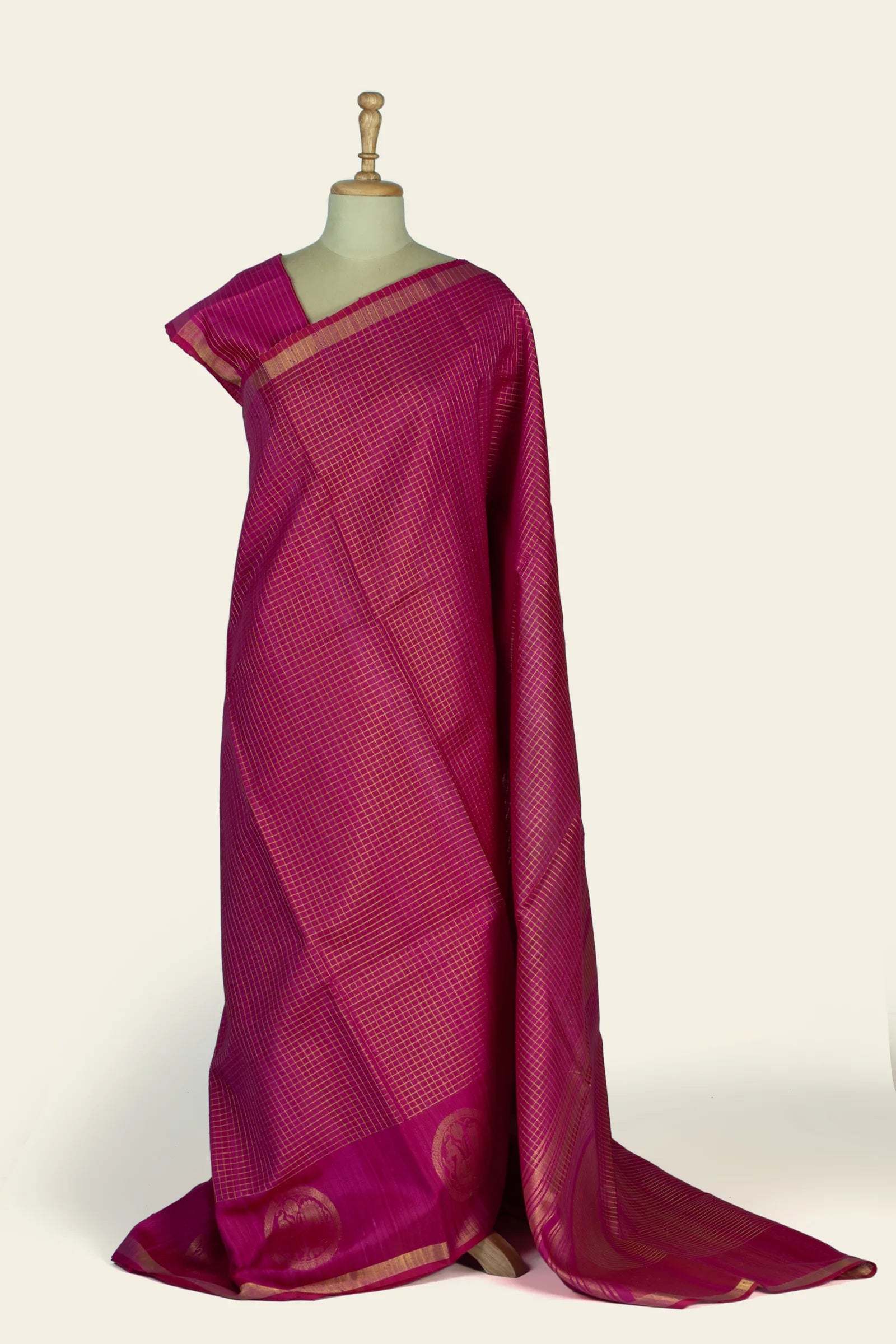 Full-length front drape of a magenta pink saree on a dress form showing an all-over small checked grid and a gold-bordered hem with circular buta near the base.